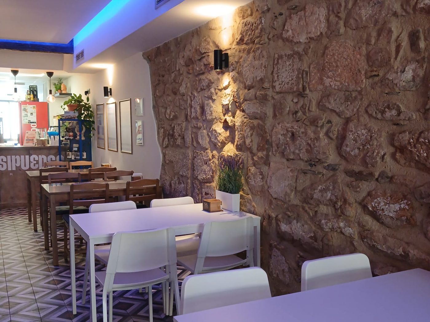Interior del restaurante Salsipuedes Burger en Baños de la Encina: pared de piedra original, mesas blancas y suelo hidráulico